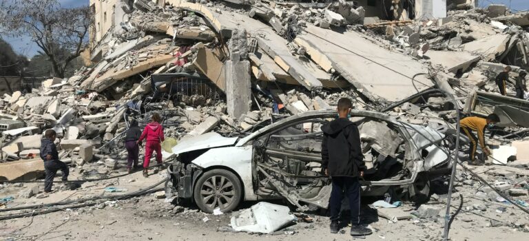 People in Gaza looking at a a destroyed building as a result of war.